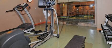 A gym with exercise equipment, a bench, and a view of a pool through a glass wall.