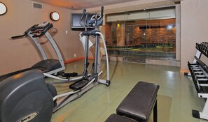 A gym with exercise equipment, a bench, and a view of a pool through a glass wall. - Banff Caribou Lodge and Spa (Banff)