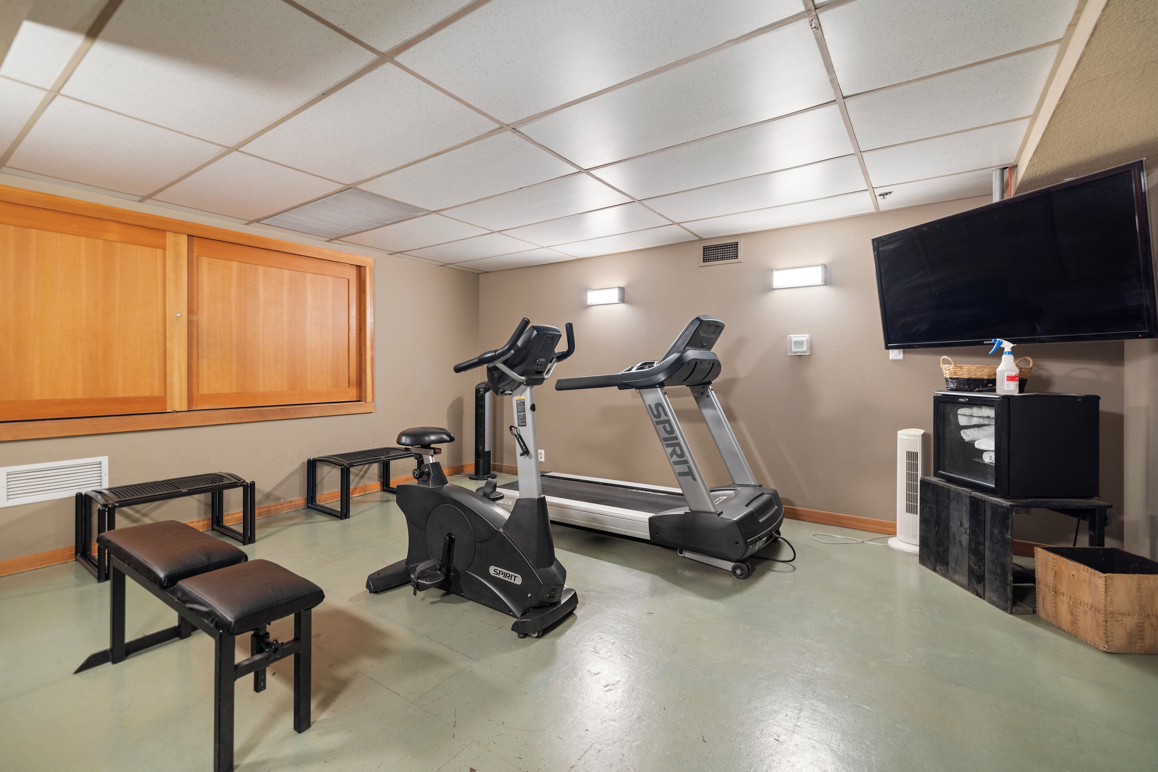 A gym with treadmills, benches, a television, and a wall-mounted heater.