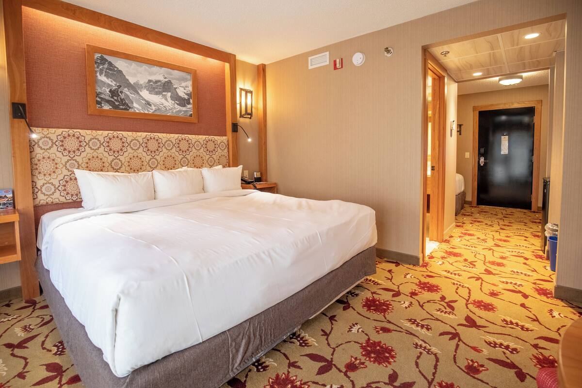 Habitación de hotel con una cama grande, cabecera con diseño estampado, un cuadro en la pared y piso alfombrado.