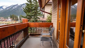 A balcony with wooden railings, two chairs, and a view of mountains and buildings in the background.