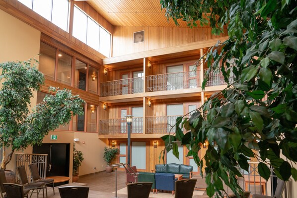 En fleretages atrium med træpaneler, et siddeområde med stole og en sofa, samt krukkeplanter.