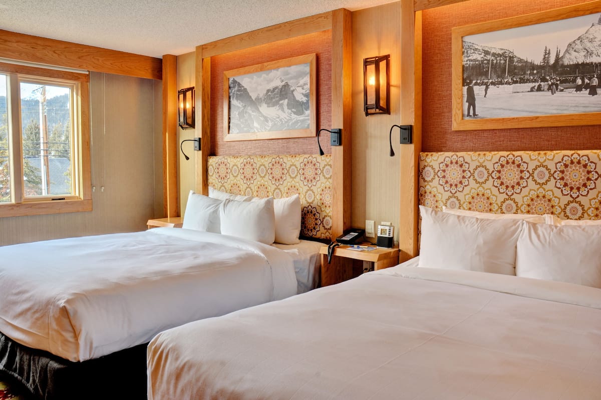 Habitación de hotel con dos camas, cabeceros de madera y cuadros en las paredes.