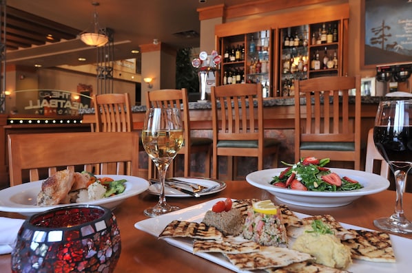 Une salle de restaurant avec un bar en arrière-plan, des chaises en bois et différents plats disposés sur la table.