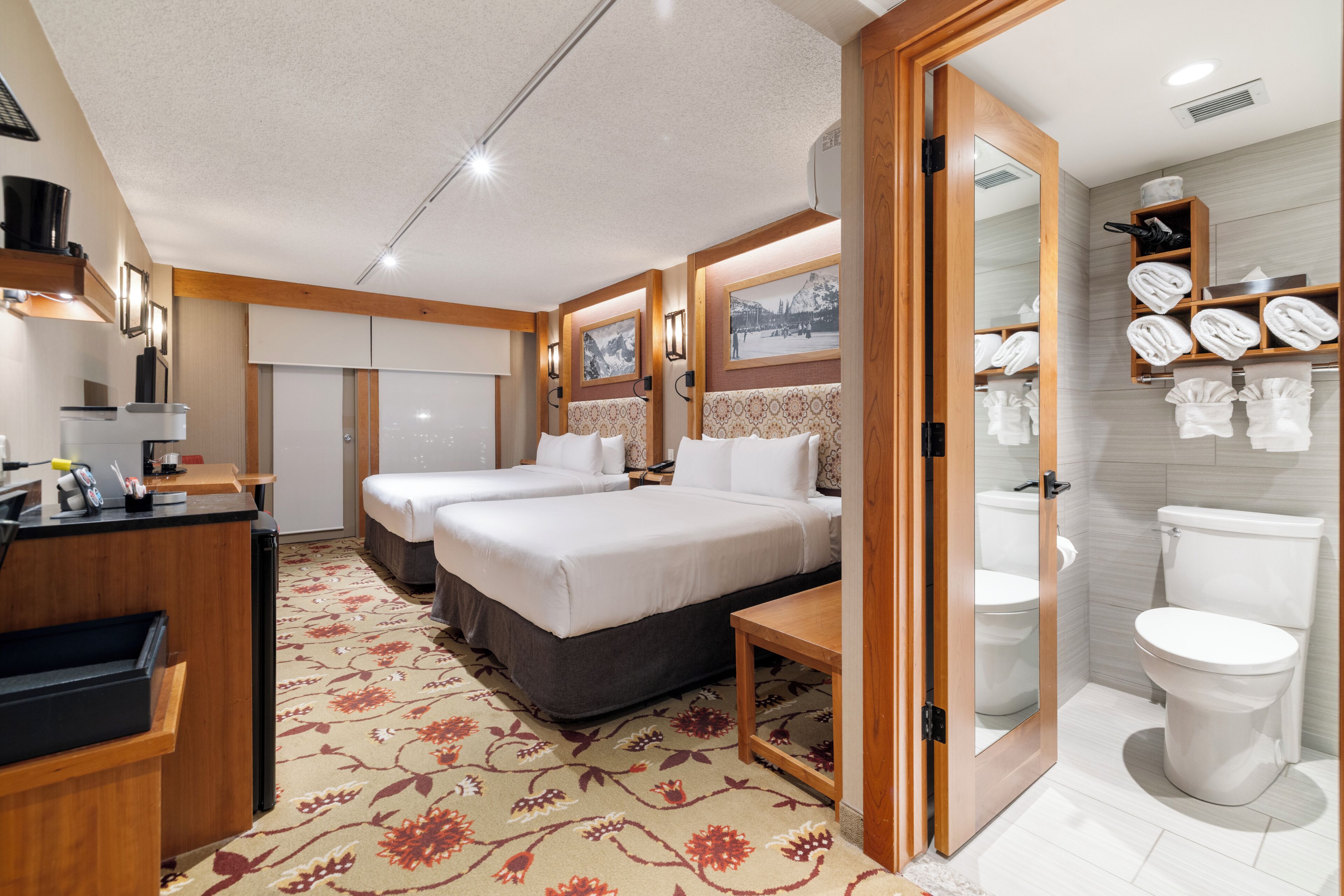 Habitación de hotel con cama, mesitas de noche, escritorio y baño con inodoro y toallero.