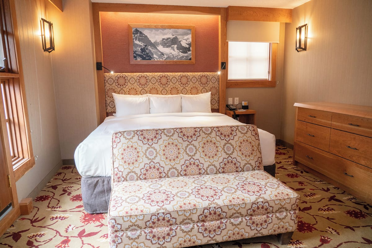 Un dormitorio con una cama grande, un banco, un aparador y un cuadro en la pared.