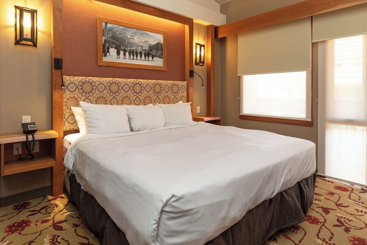 Habitación de hotel con una cama grande, cabecera de madera, un cuadro en la pared y un teléfono en la mesita de noche.