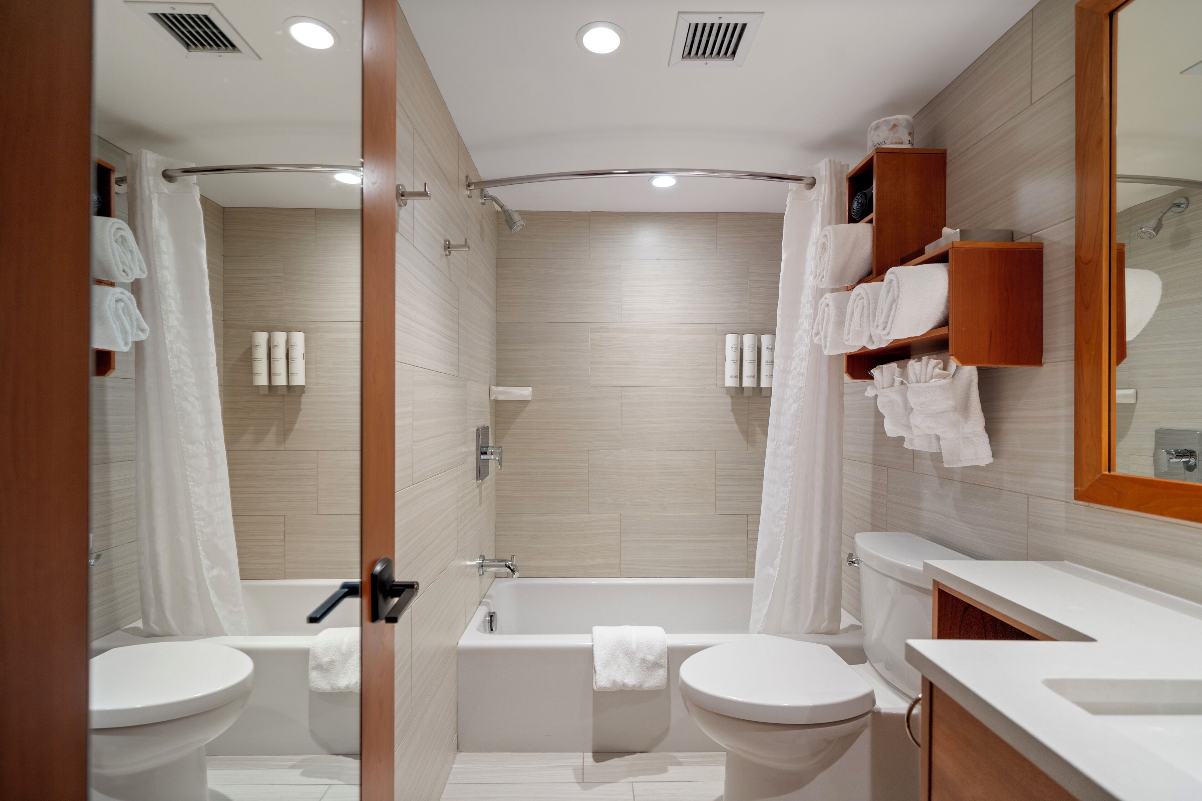 A modern bathroom with a bathtub, two toilets, and a vanity with a mirror.