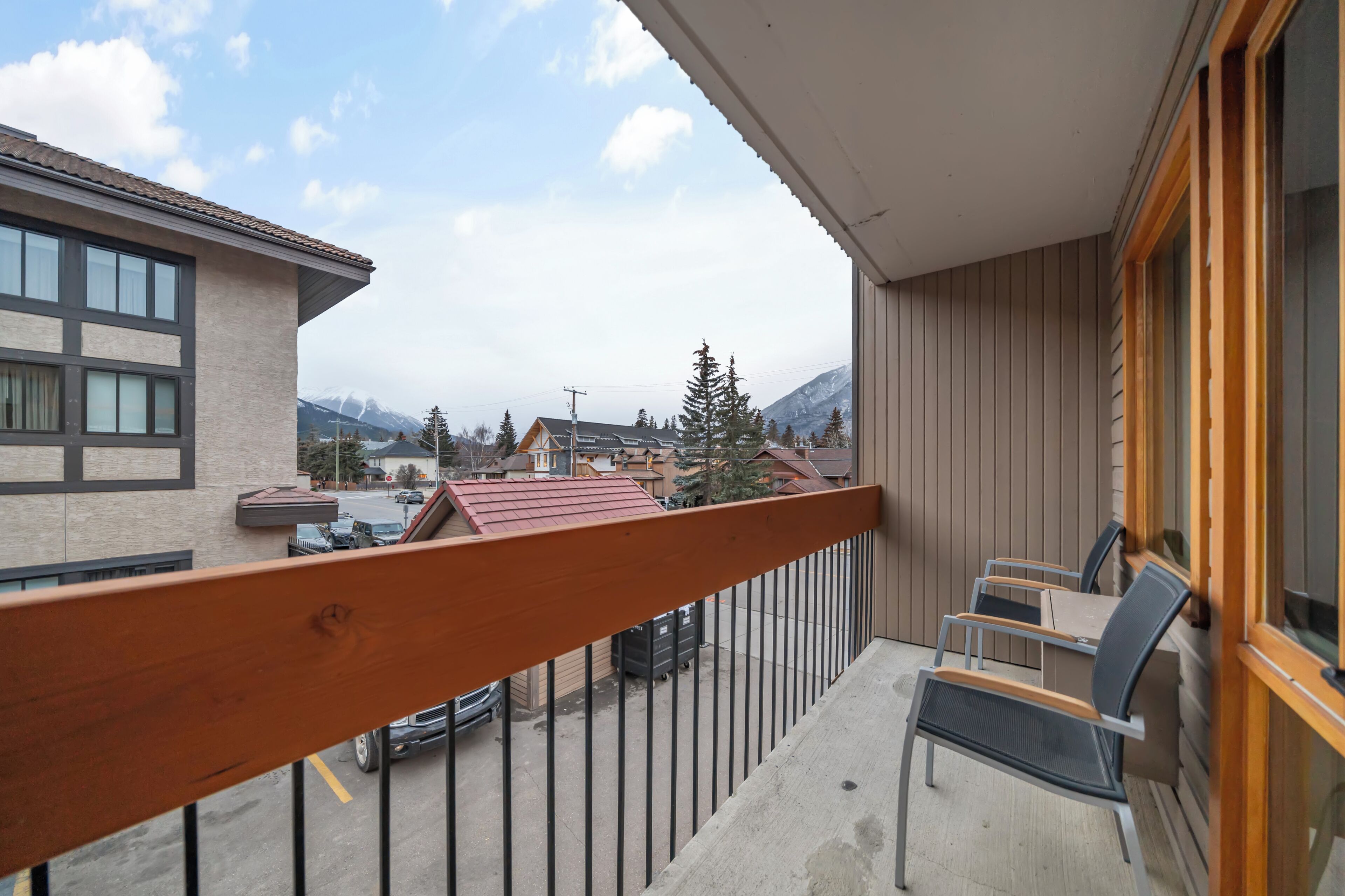A balcony with a view of a mountain, a parked car, and a building with a tiled roof.