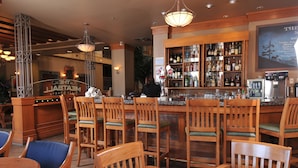 A bar area with wooden chairs and tables, a bar counter with a variety of bottles, and a menu on the wall.