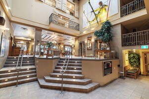 Un vestíbulo de hotel de varios niveles con una escalera central, un mostrador de recepción y una gran planta de interior.