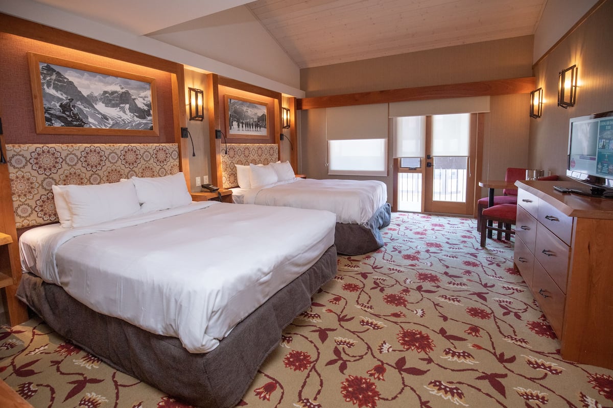 Habitación de hotel con dos camas, un televisor, un escritorio con silla y un balcón con vistas.