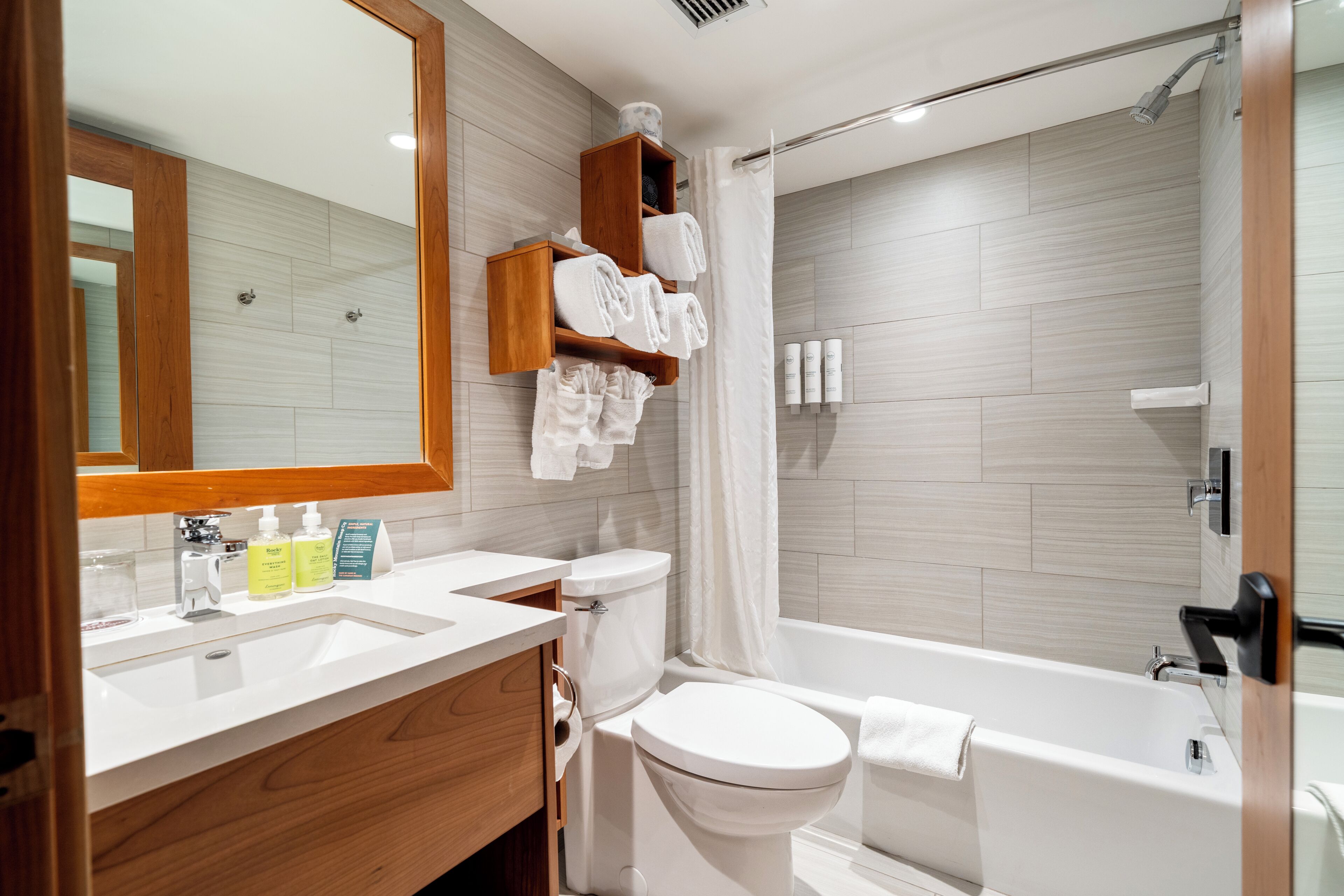 A modern bathroom with a wooden vanity, a toilet, a bathtub, and a shower.