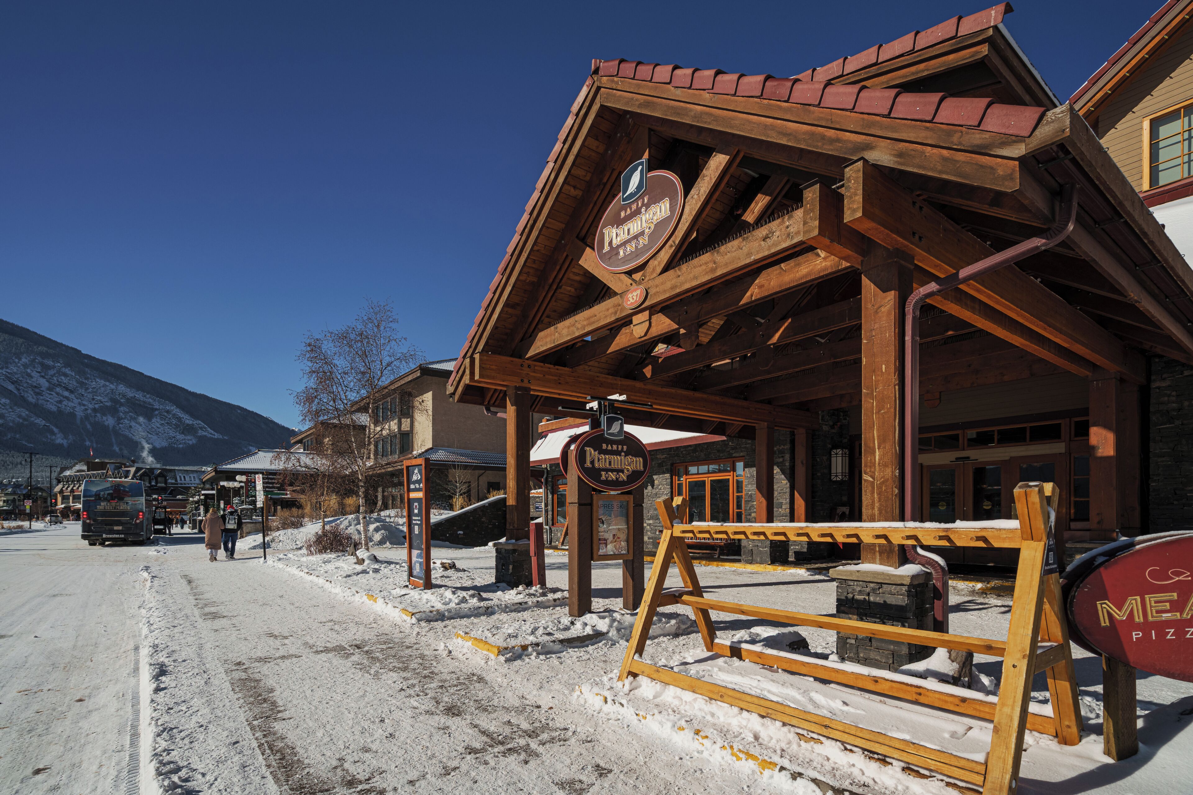 A wooden building with a sign for Parmigan Inn, a wooden bench, and a snow-covered ground.