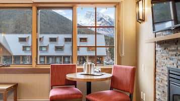 Un comedor con una mesa y dos sillas, una ventana con vistas a edificios y montañas, y una chimenea de ladrillo.