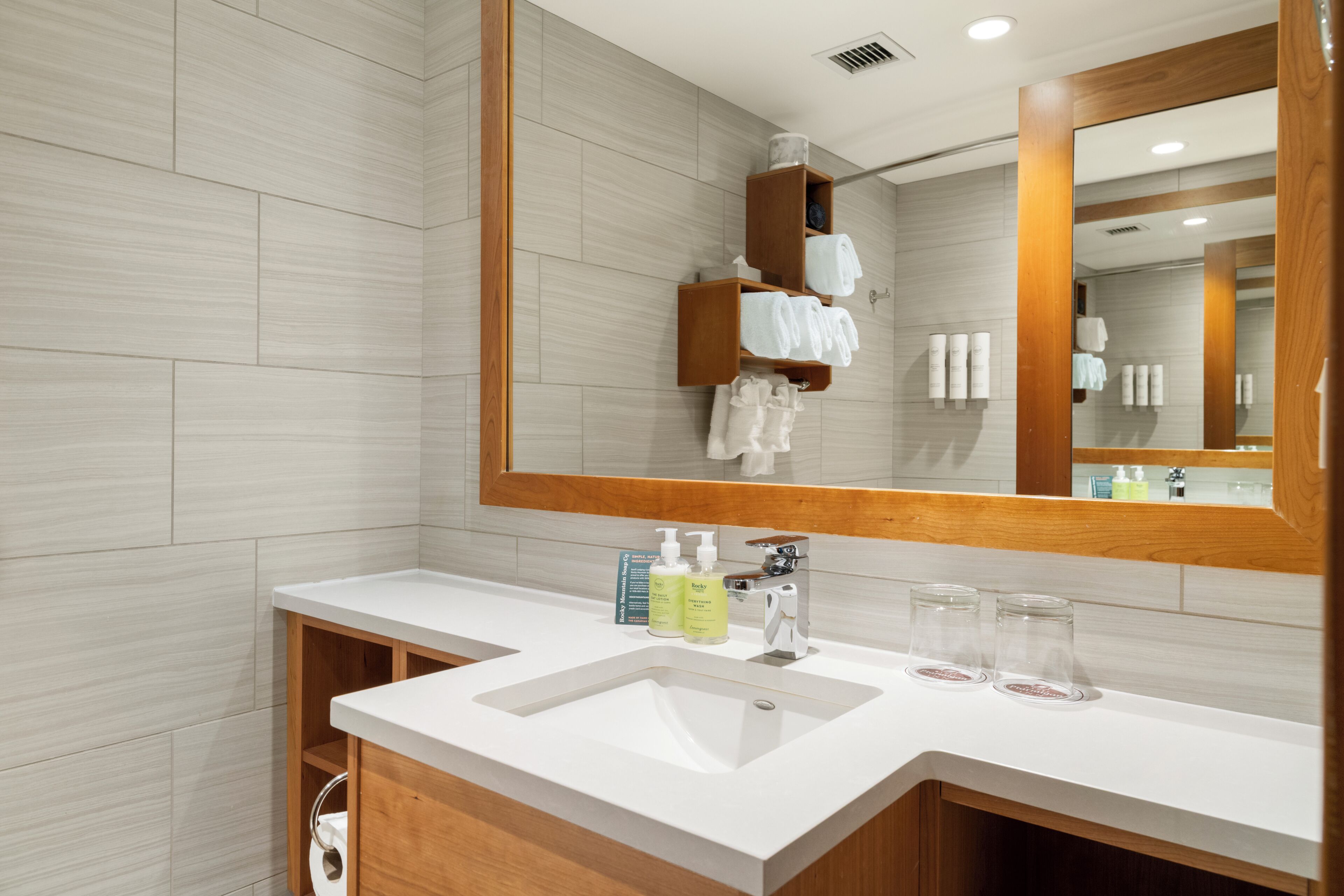 A modern bathroom with a large mirror, a white sink, and a wooden vanity.