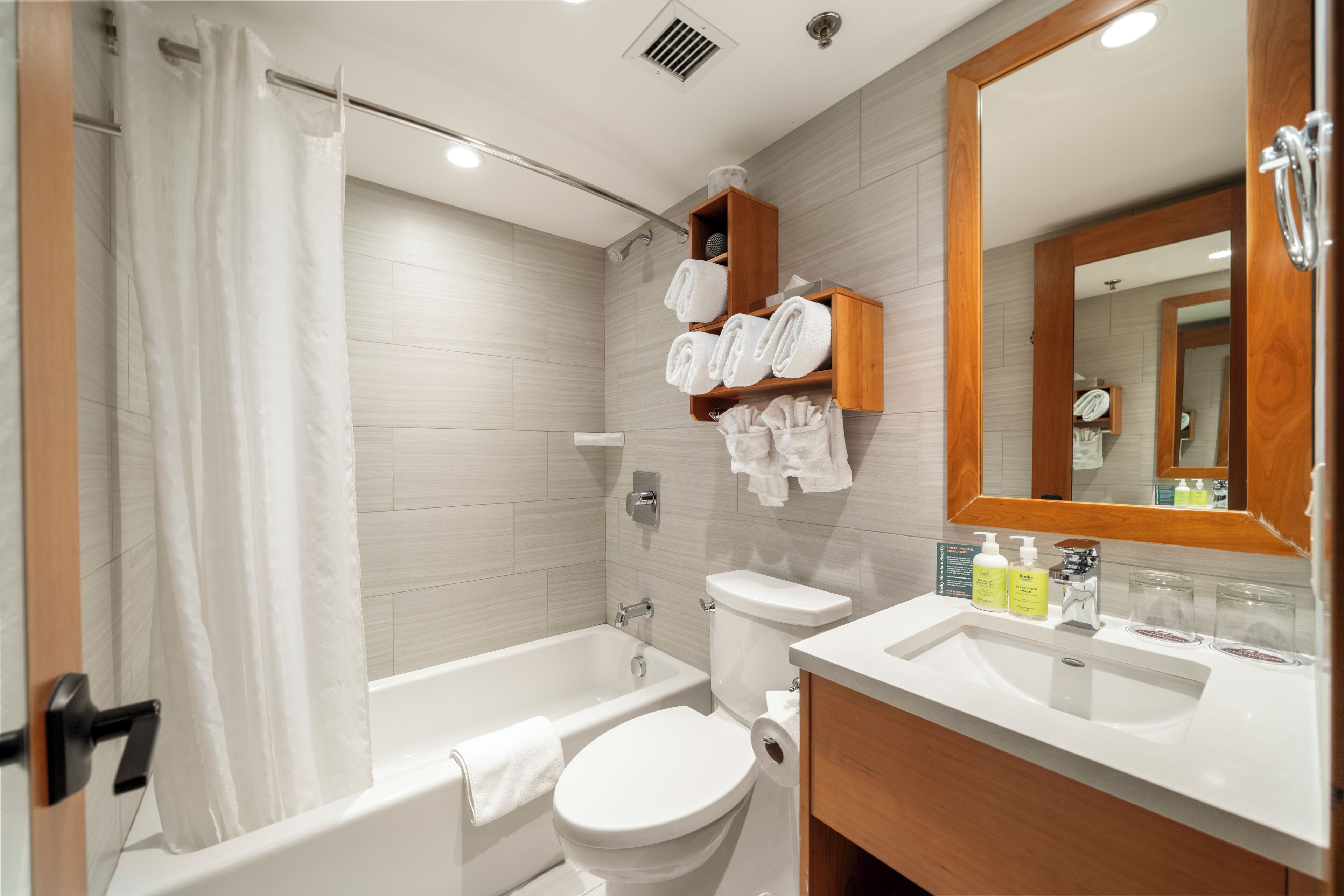 A modern bathroom with a bathtub, toilet, and sink. There are towels and toiletries on the shelves.