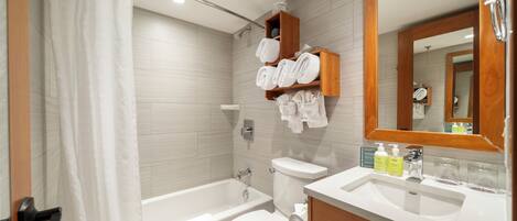 A modern bathroom with a bathtub, toilet, and sink. There are towels and toiletries on the shelves.