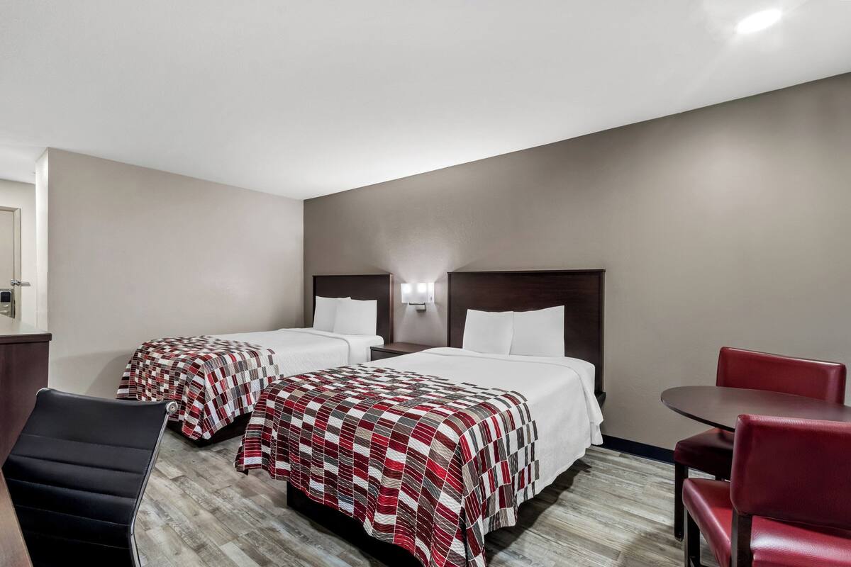 A hotel room with two beds, a desk, and a chair.