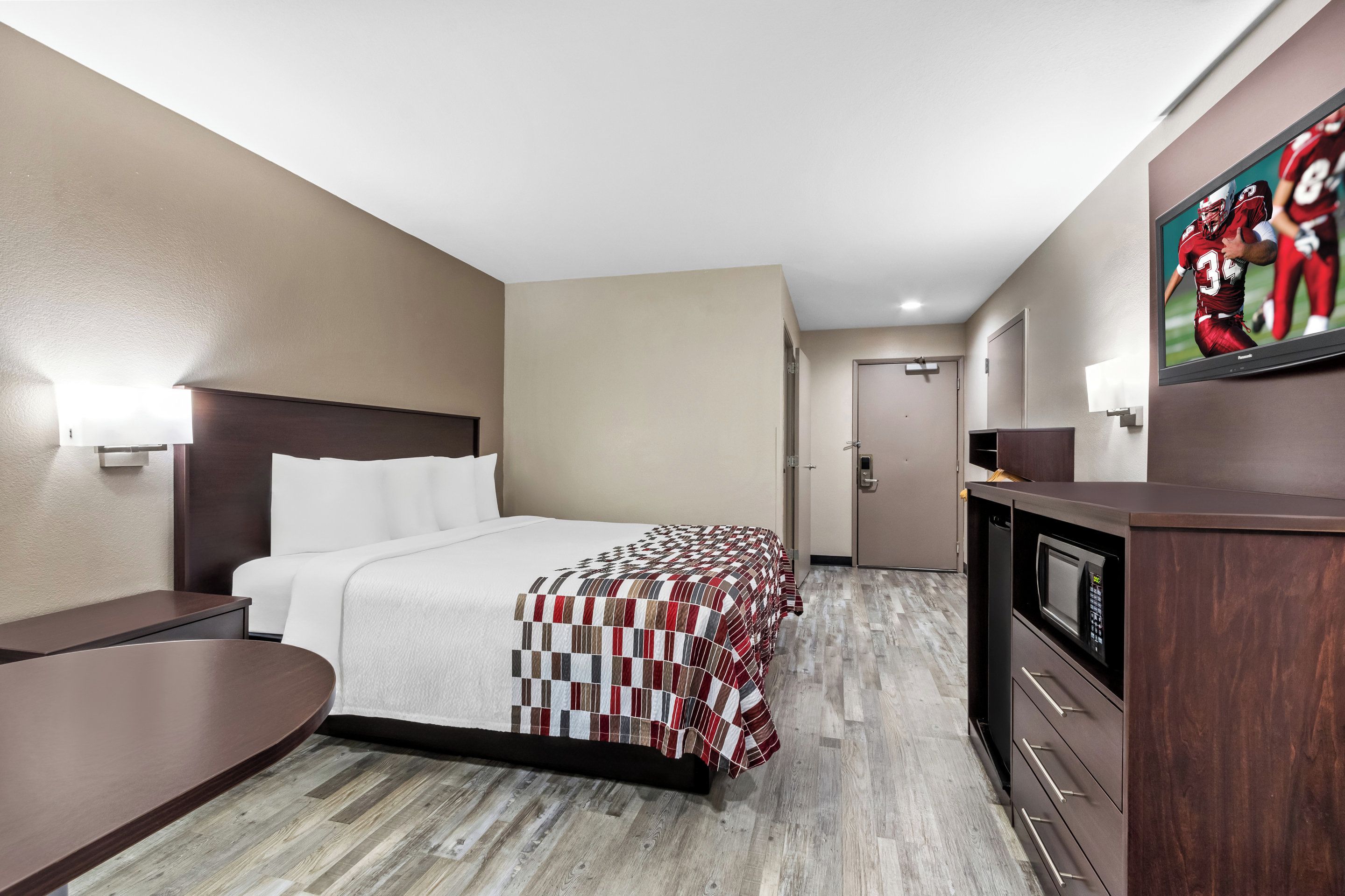 A hotel room with a bed, a desk, a microwave, and a TV.