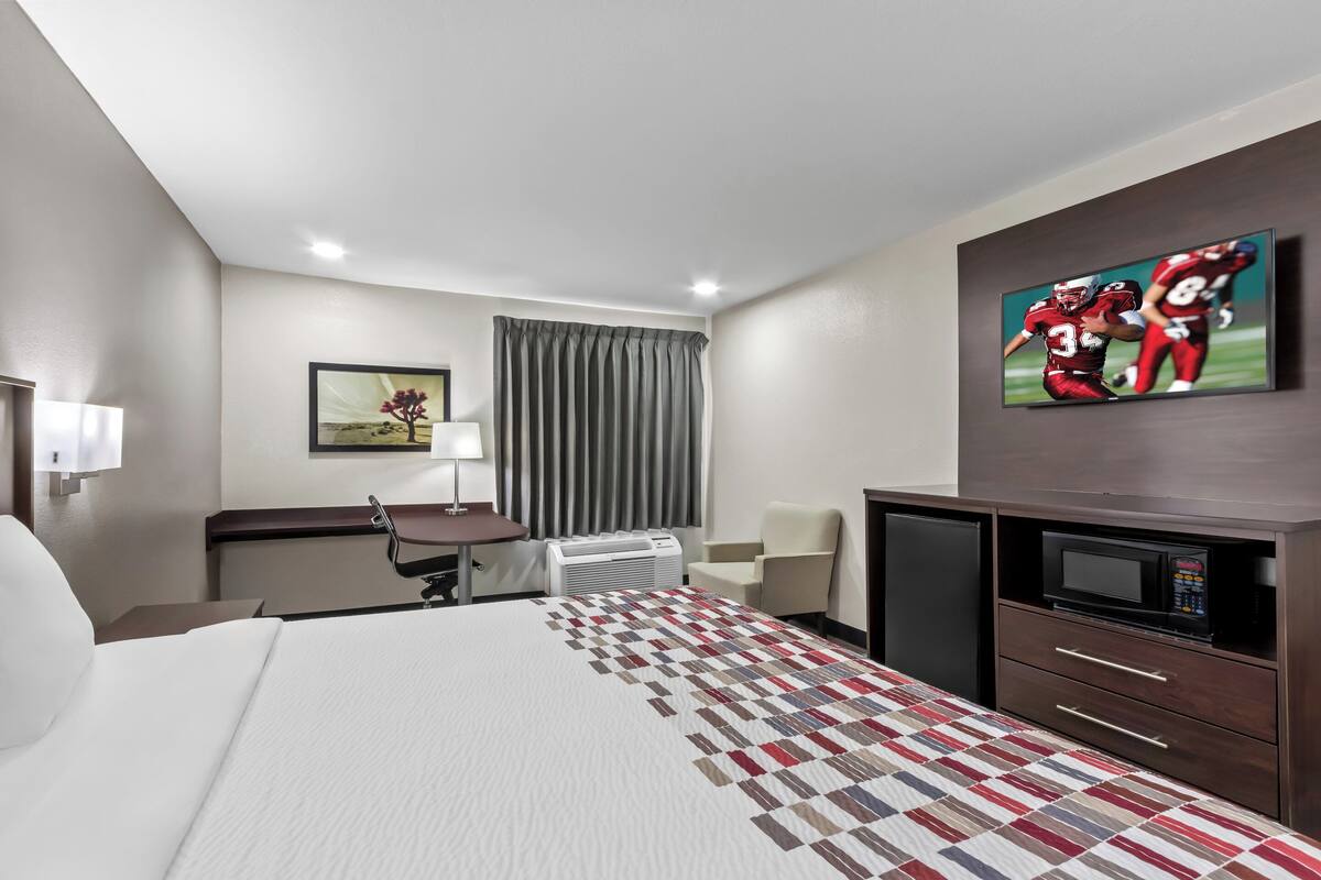 A hotel room with a bed, a desk, a chair, a television, and a microwave.