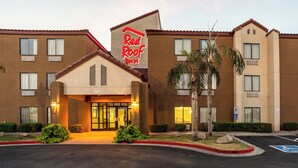 Un hôtel Red Roof Inn au design moderne, avec une entrée bien visible dotée de portes en verre, un parking et un panneau indiquant clairement les places de stationnement réservées aux personnes handicapées.
