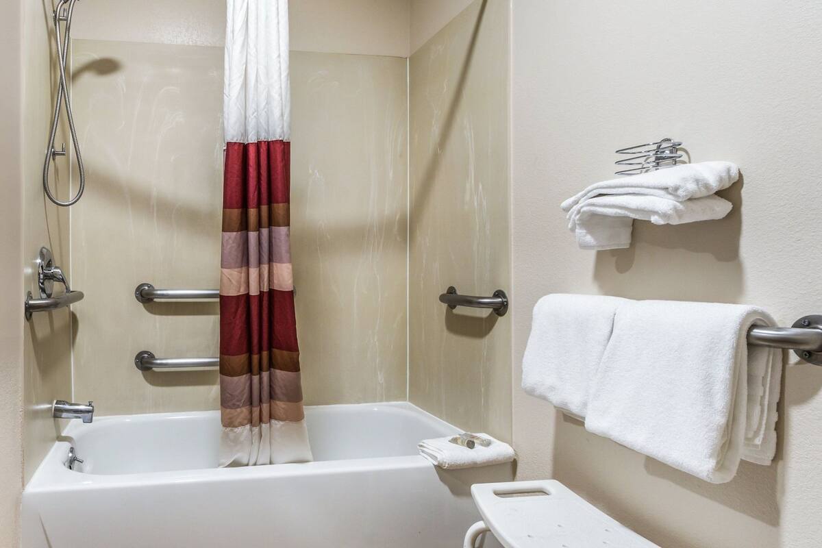 A bathroom with a bathtub, a shower curtain, a towel rack, and a small shelf with towels.