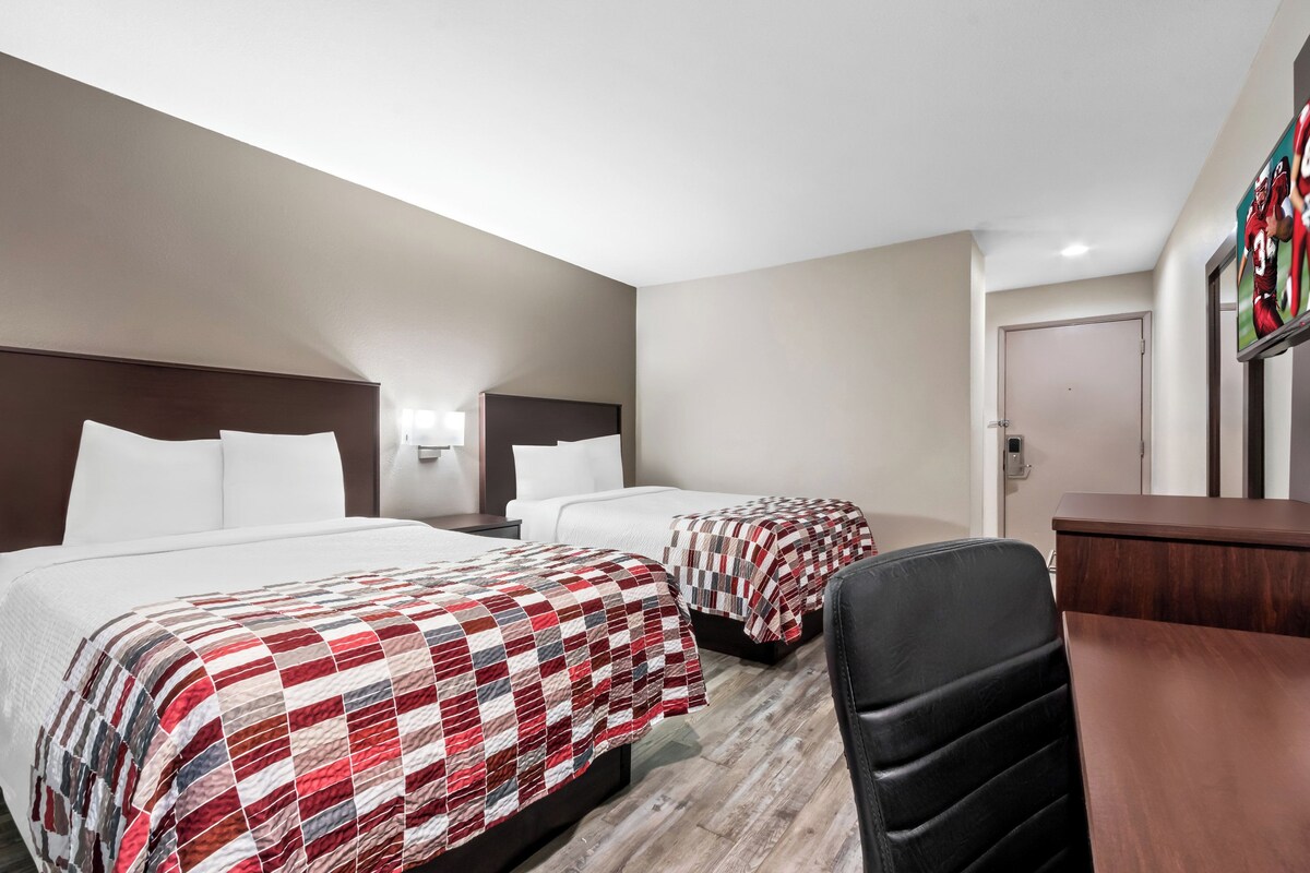 A hotel room with two beds, a desk, and a chair.