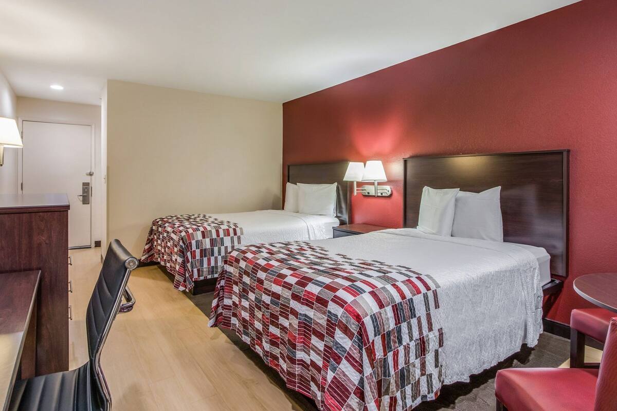 A hotel room with two beds, a desk, a chair, and a small table.