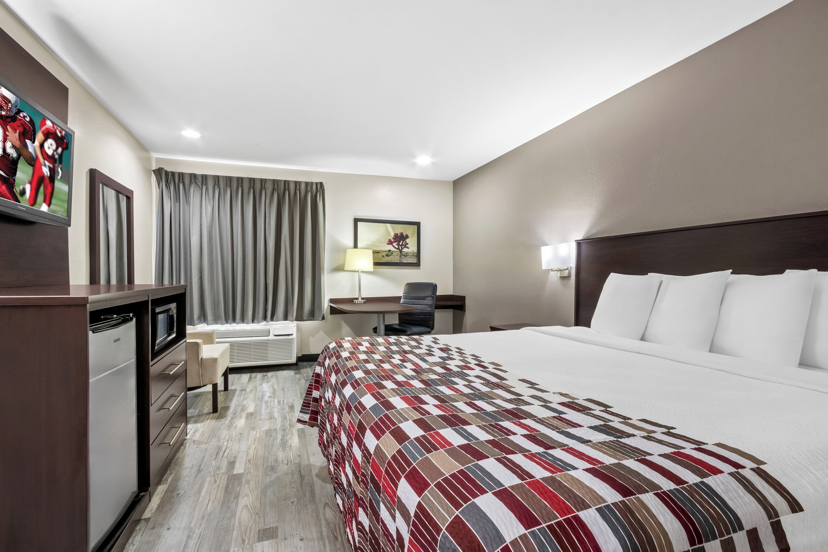 Una habitación de hotel con una cama grande, un escritorio, una silla, un televisor y un mini bar.