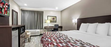 A hotel room with a large bed, a desk, a chair, a TV, and a minibar.