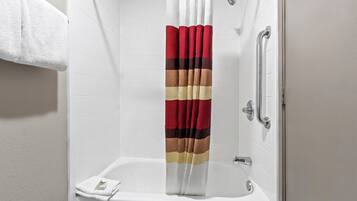 A shower with a white tiled wall, a red and beige striped shower curtain, and a white towel on the floor.