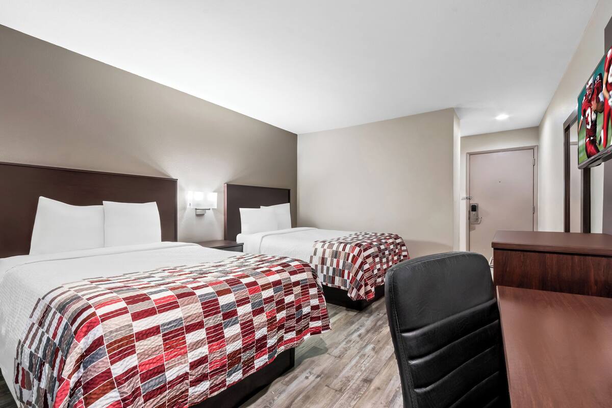A hotel room with two beds, a desk, and a chair.
