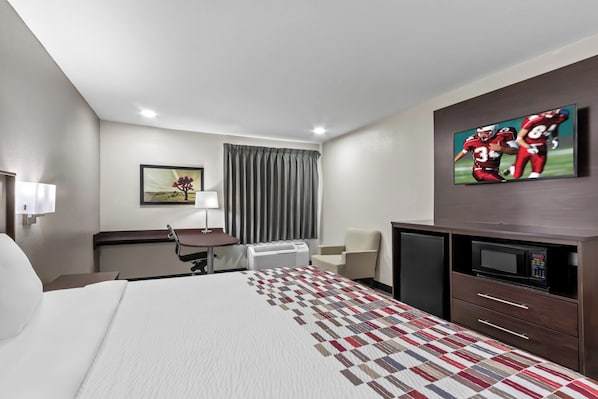 Ett hotellrum med en säng, ett skrivbord, en stol, en tv och en mikrovågsugn.