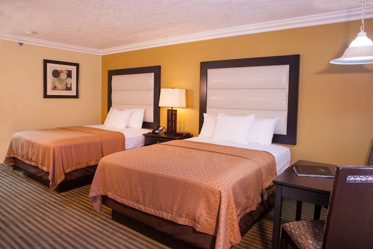 A hotel room with two beds, a bedside table with a lamp, and a framed picture on the wall.