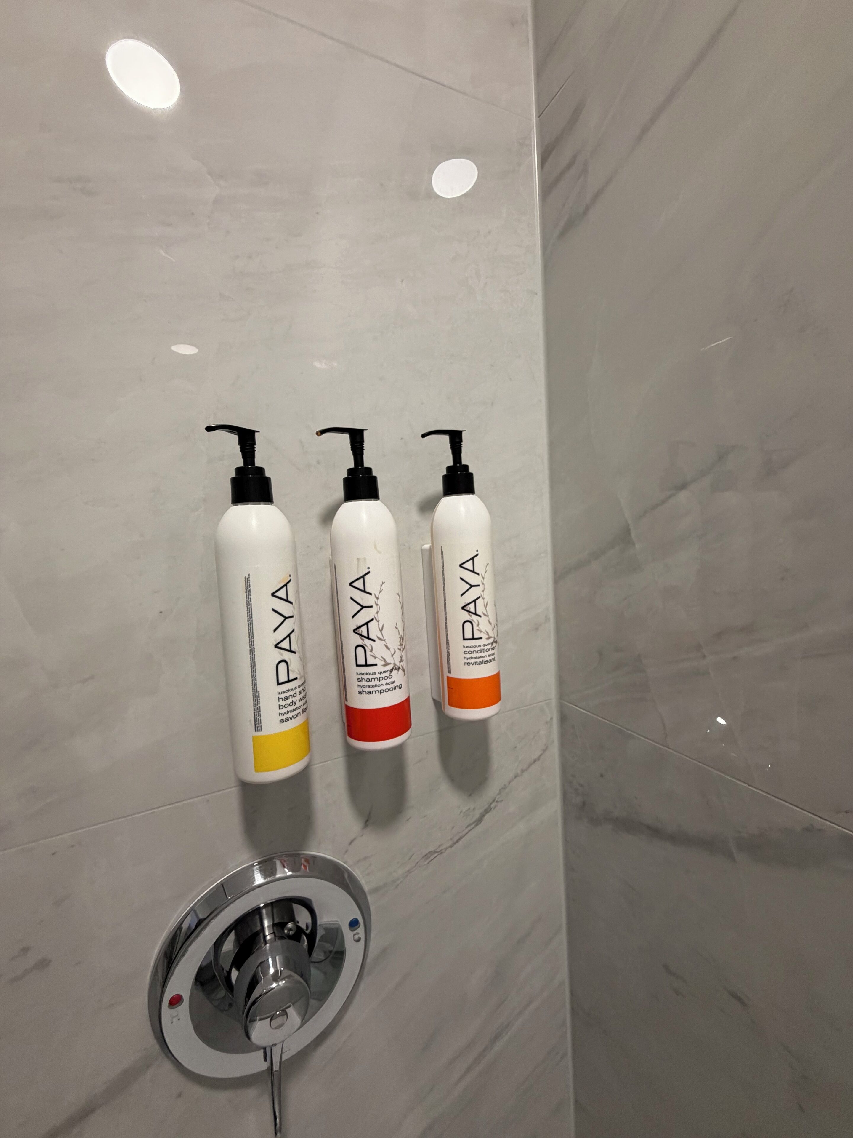 Tres botellas de champú Paya sobre una pared de mármol.