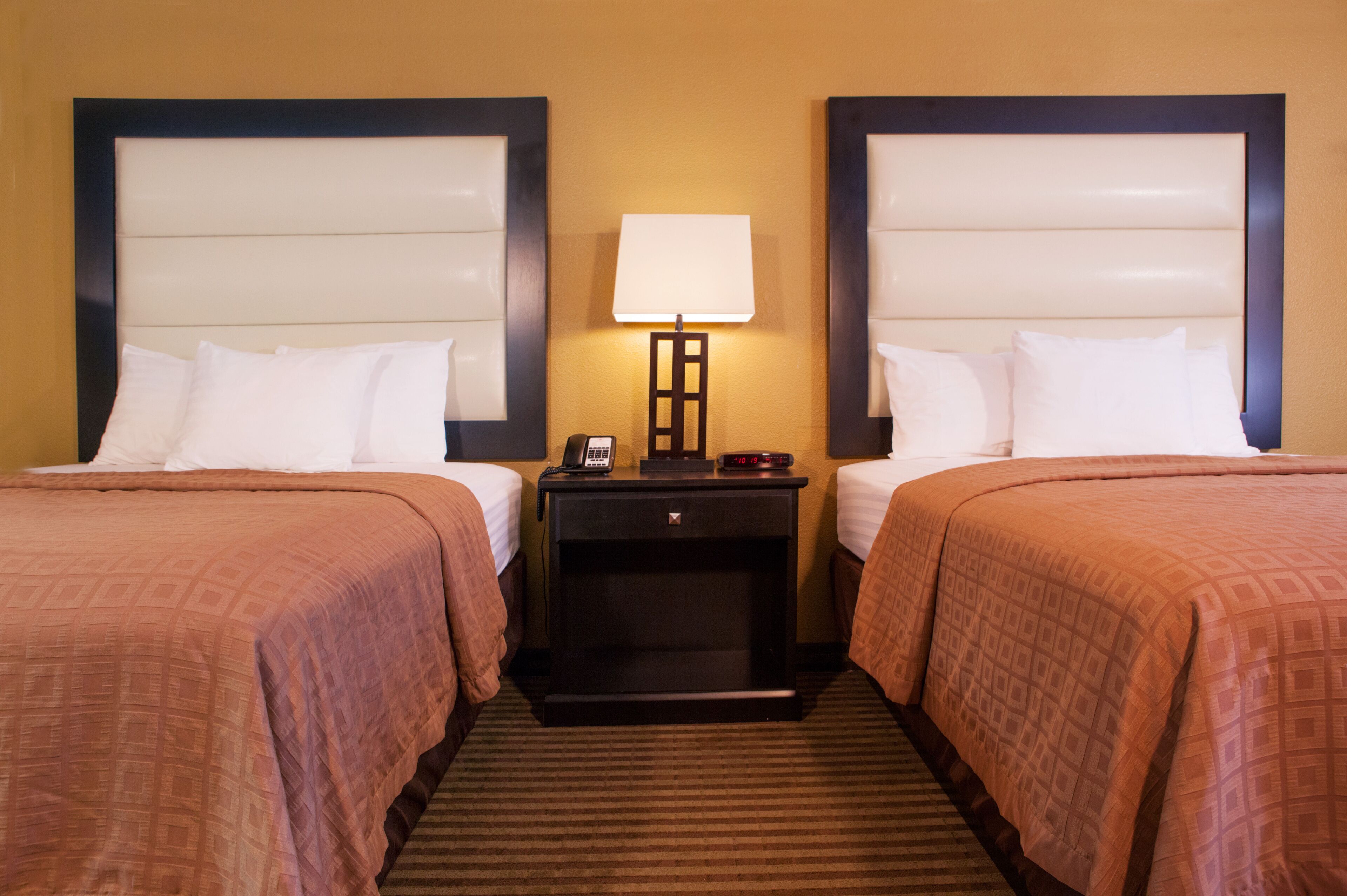 Een hotelkamer met twee bedden, een nachtkastje met een lamp en een klein tafeltje.