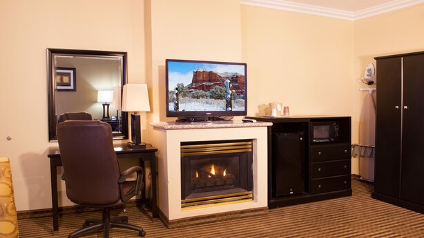 Habitación de hotel con televisor, chimenea, escritorio con lámpara, una silla y armario.