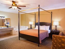 Una habitación de hotel con una cama con dosel, una zona de estar con una silla, un tocador con espejo y un ventilador de techo.
