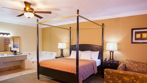 Una cama con dosel y cabecera, dos mesitas de noche con lámparas, una silla y un baño con lavamanos y espejo.