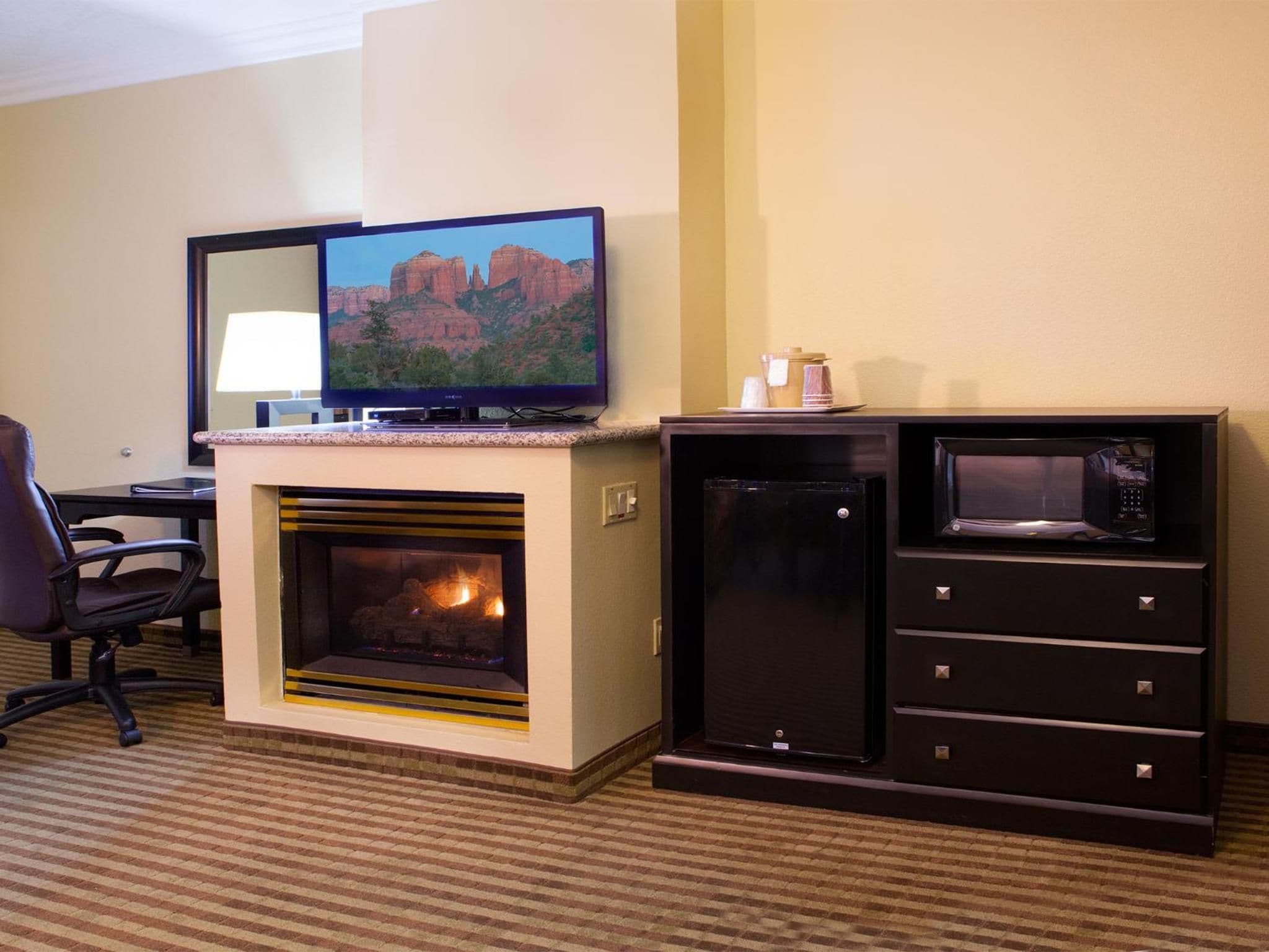 Une chambre d’hôtel équipée d’une cheminée, d’une télévision, d’un four à micro-ondes et d’un bureau avec une chaise.