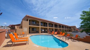 Un hotel con zona de piscina, mobiliario exterior y un edificio de varios pisos con balcones.