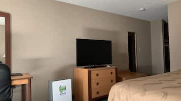 Une chambre d’hôtel avec un lit, un téléviseur posé sur une commode en bois, un bureau avec une chaise et un petit réfrigérateur.