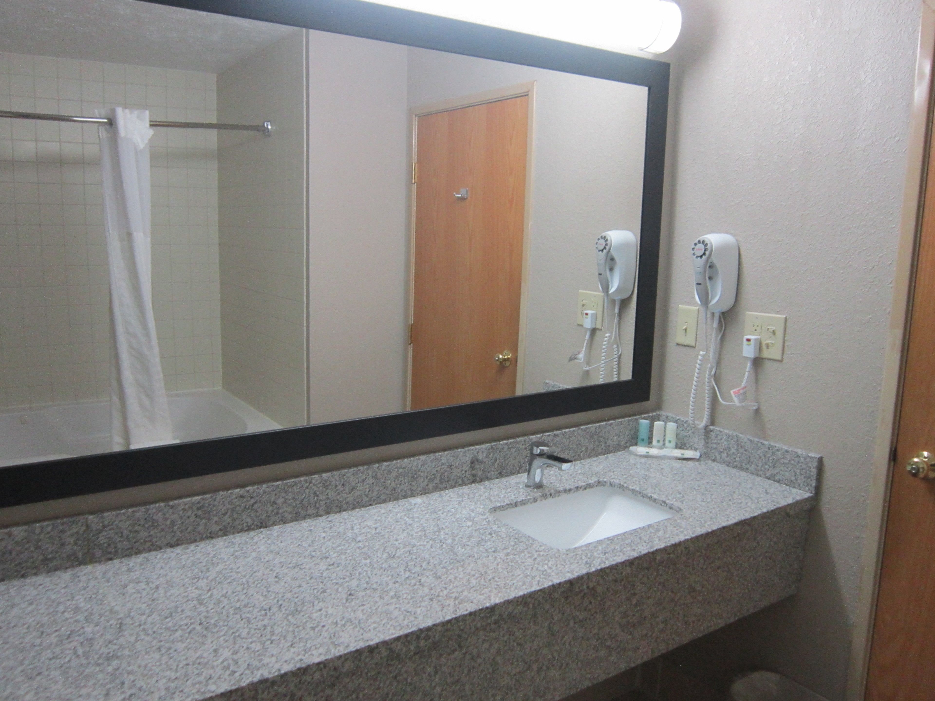Une salle de bain avec un grand miroir, un lavabo et un sèche-cheveux fixé au mur.