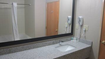 Une salle de bain avec un grand miroir, un lavabo et un sèche-cheveux fixé au mur.
