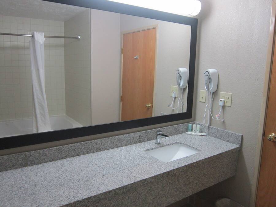 Une salle de bain avec un grand miroir, un lavabo et un sèche-cheveux fixé au mur.