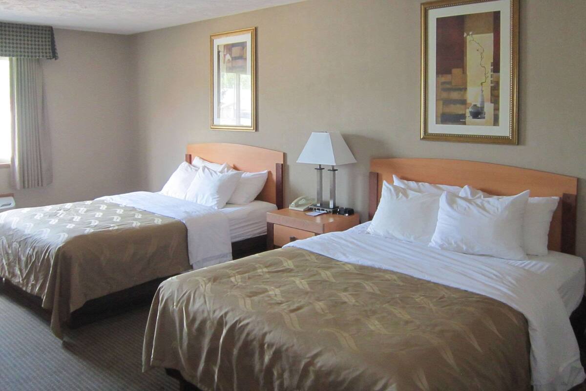 A hotel room with two beds, a nightstand with a lamp, and framed artwork on the walls.