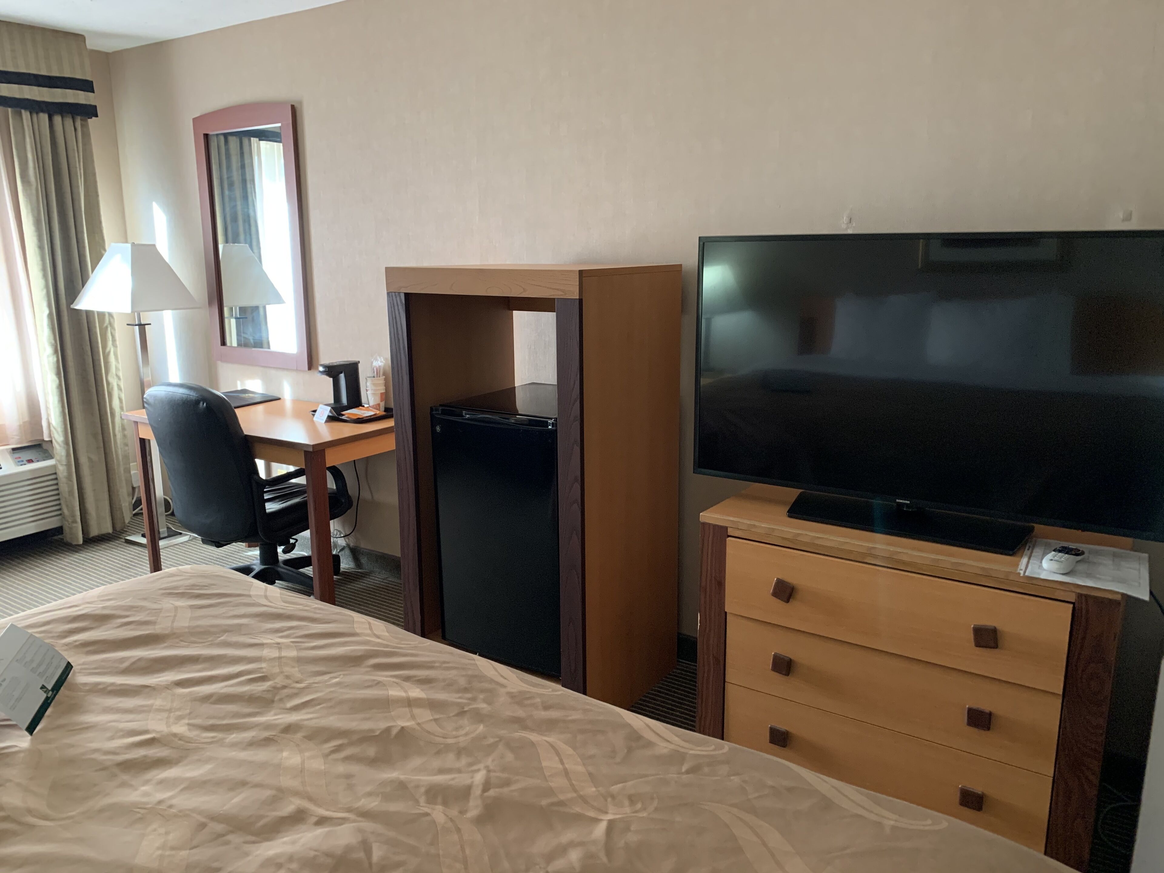 A hotel room with a bed, a desk, a television, and a minibar.