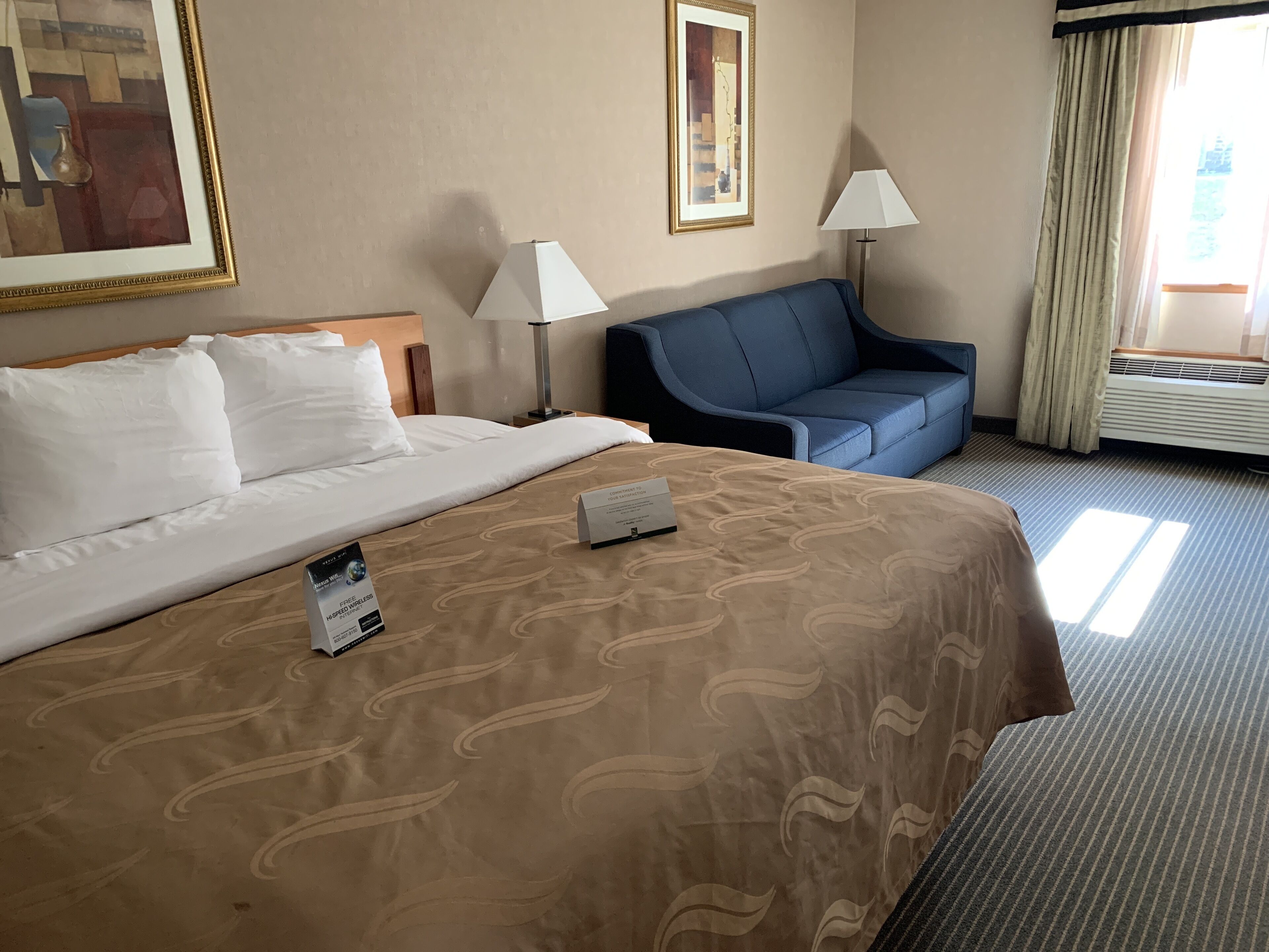 A hotel room with a large bed, a blue sofa, two lamps, and a framed picture on the wall.