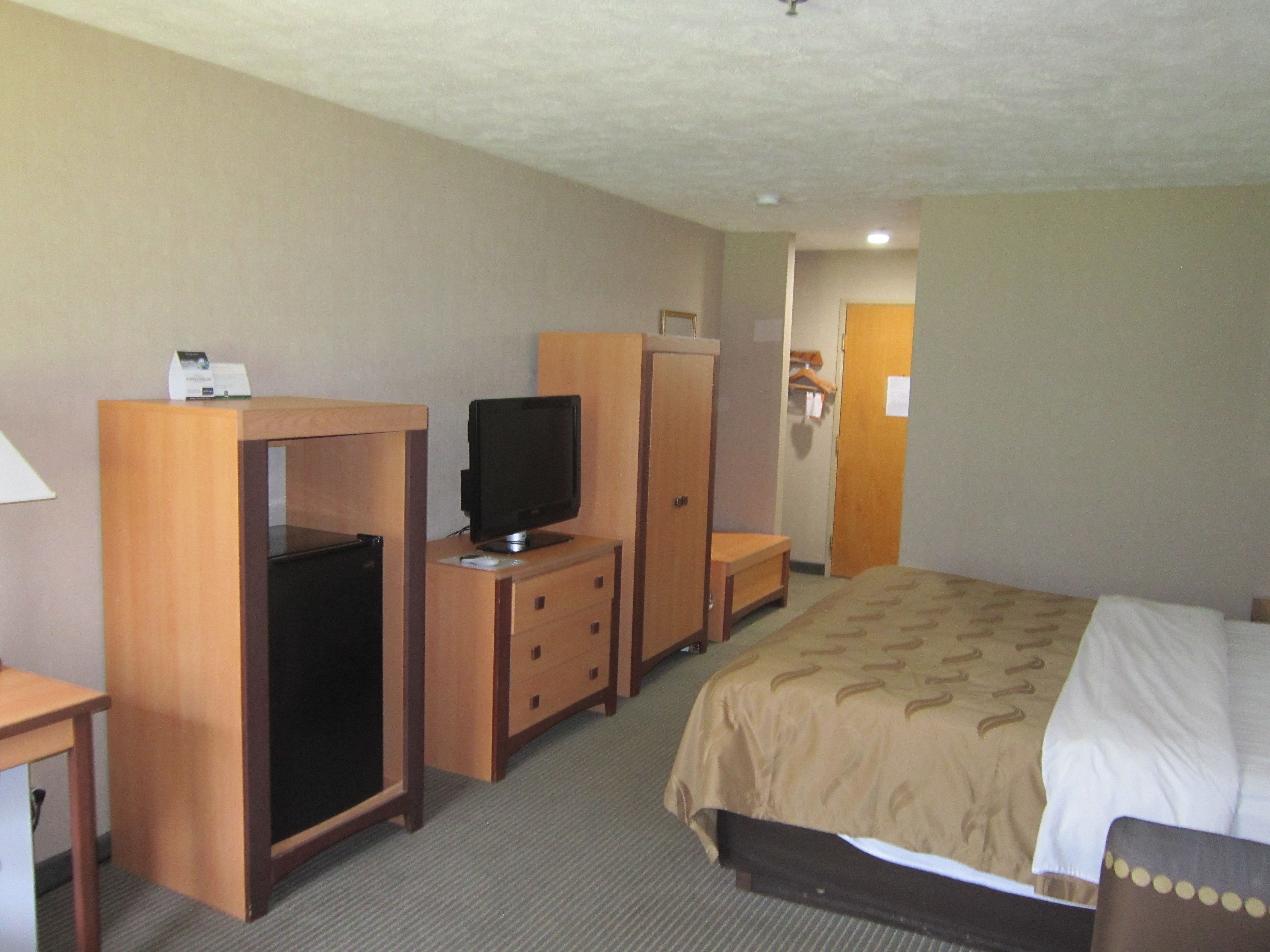 A hotel room with a bed, a desk with a computer, a television, and a wardrobe.